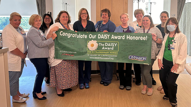 Virginia Grace standing with colleagues in front of a DAISY Award banner